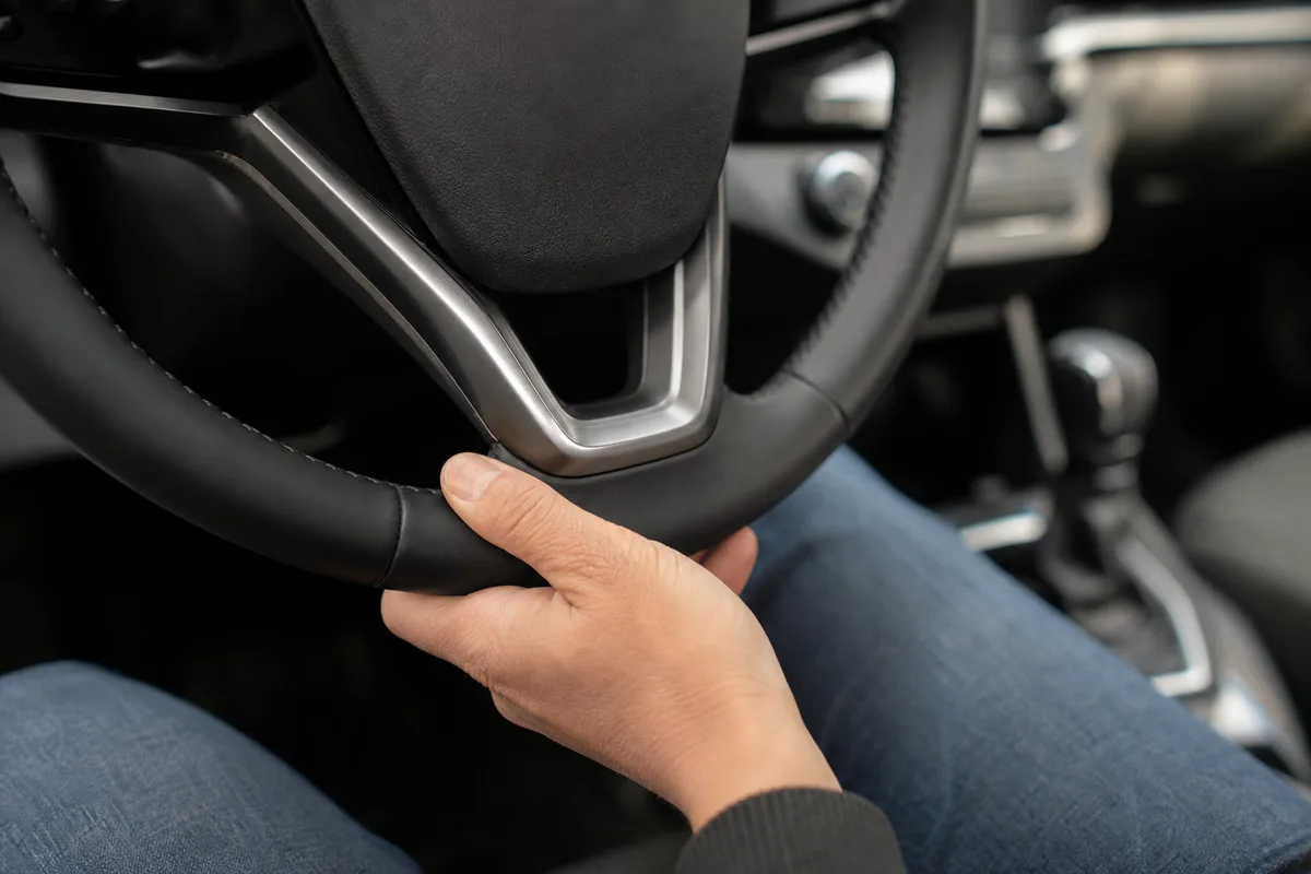 Gros plan d&rsquo;une main posée sur le bas du volant à la position 6 heures dans un habitacle de voiture